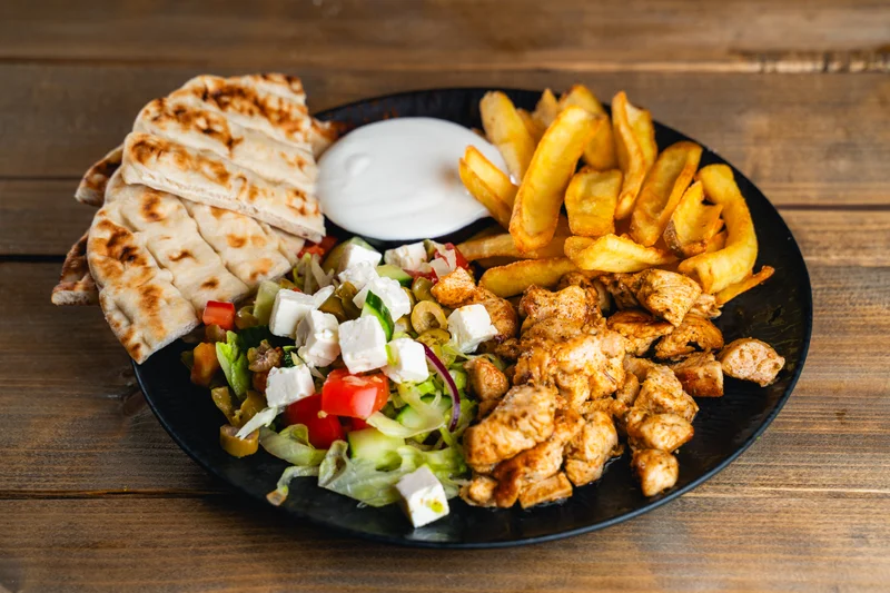 Görög Grill Tál 1 Csirke gyros tál, sült pitával és salátával és friss csónakburgonyával tálalva.